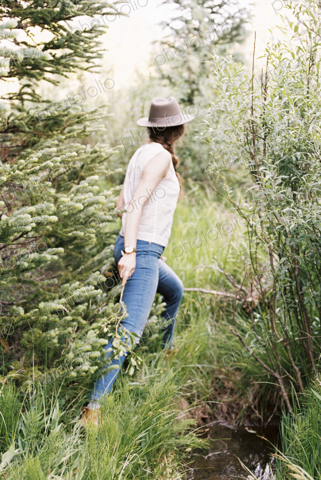 Woman wearing jeans and a hat walking through a forest.