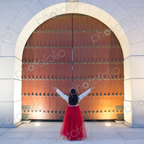 Woman wearing long red skirt standing with her arms raised under an arch Woman wearing long red skirt standing with her arms raised under an arch