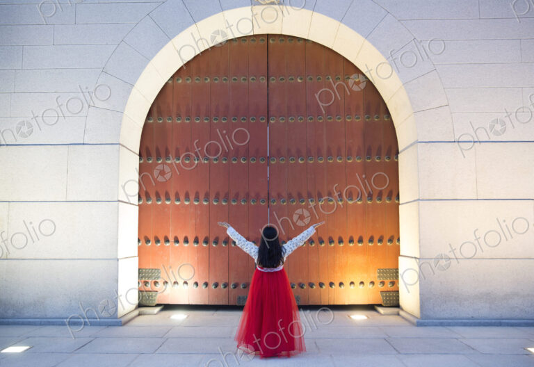 Woman wearing long red skirt standing with her arms raised under an arch