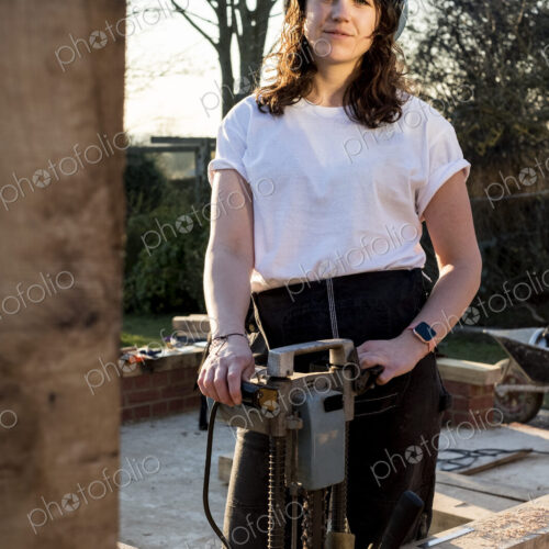 Woman wearing protective goggles holding machine, working on wooden building frame. Woman wearing protective goggles holding machine, working on wooden building frame.