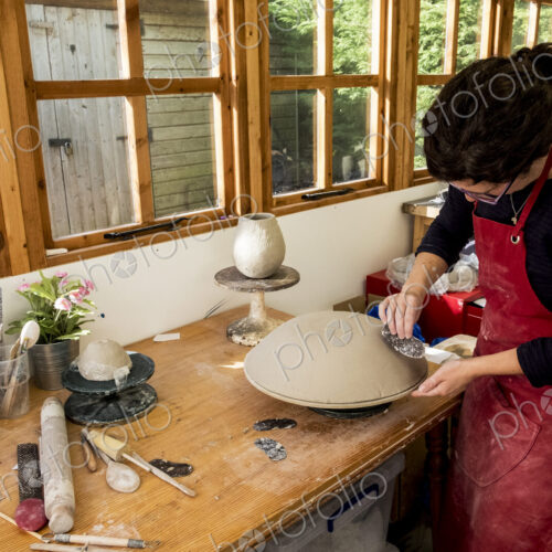 Woman wearing red apron standing in her ceramics workshop, working on clay bowl.