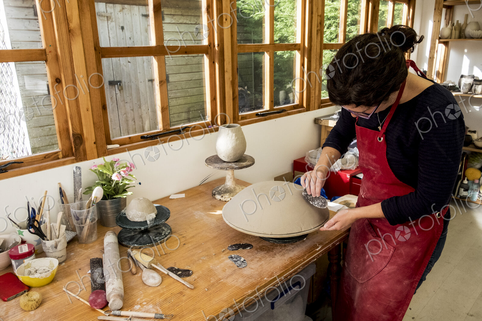 Woman wearing red apron standing in her ceramics workshop, working on clay bowl.