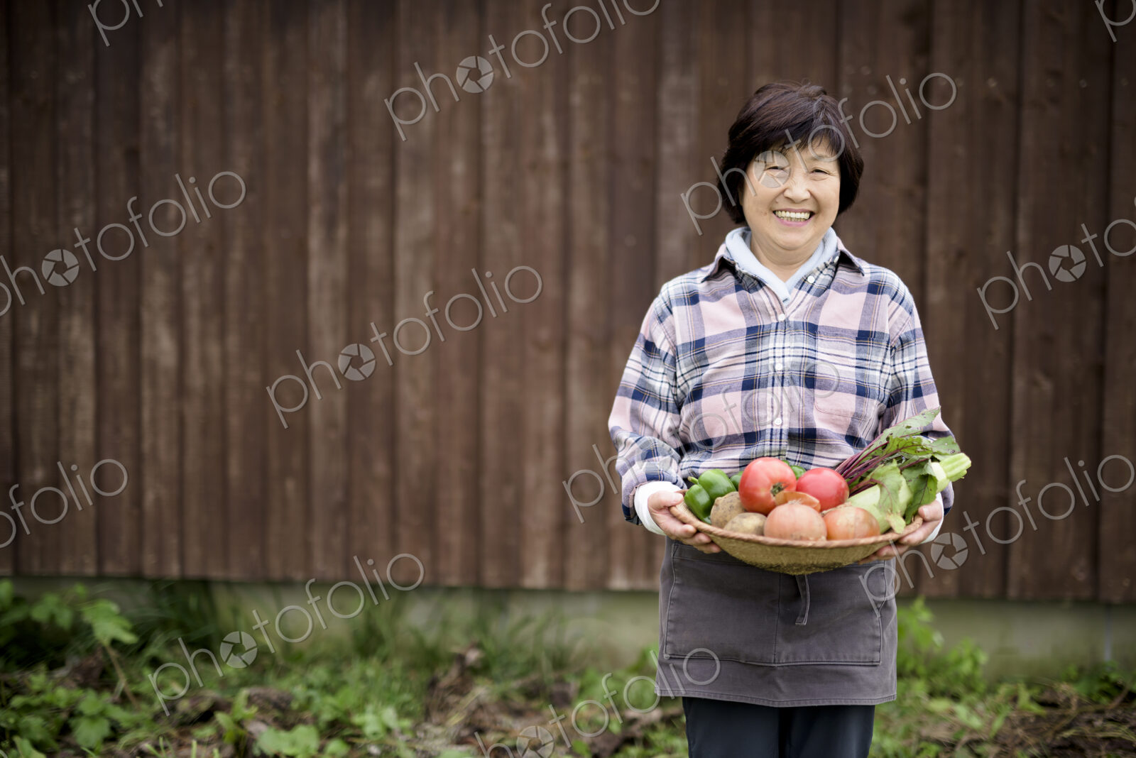 Woman with black hair wearing checkered shirt standing in a garden, holding basket…