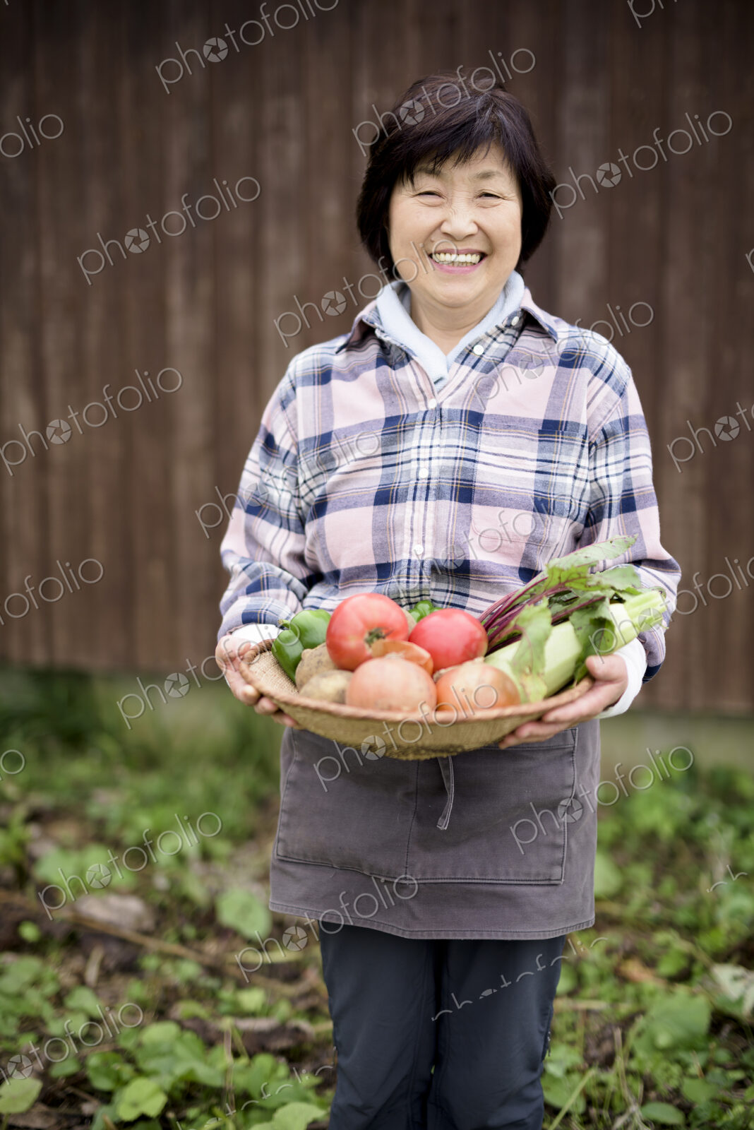 Woman with black hair wearing checkered shirt standing in a garden, holding basket…