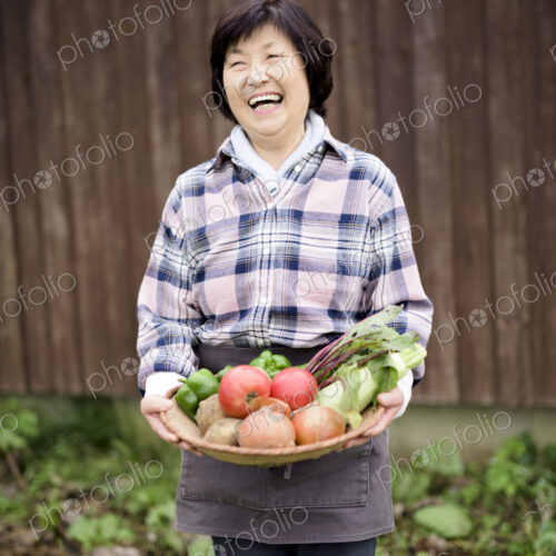 Woman with black hair wearing checkered shirt standing in a garden, holding basket… Woman with black hair wearing checkered shirt standing in a garden, holding basket…