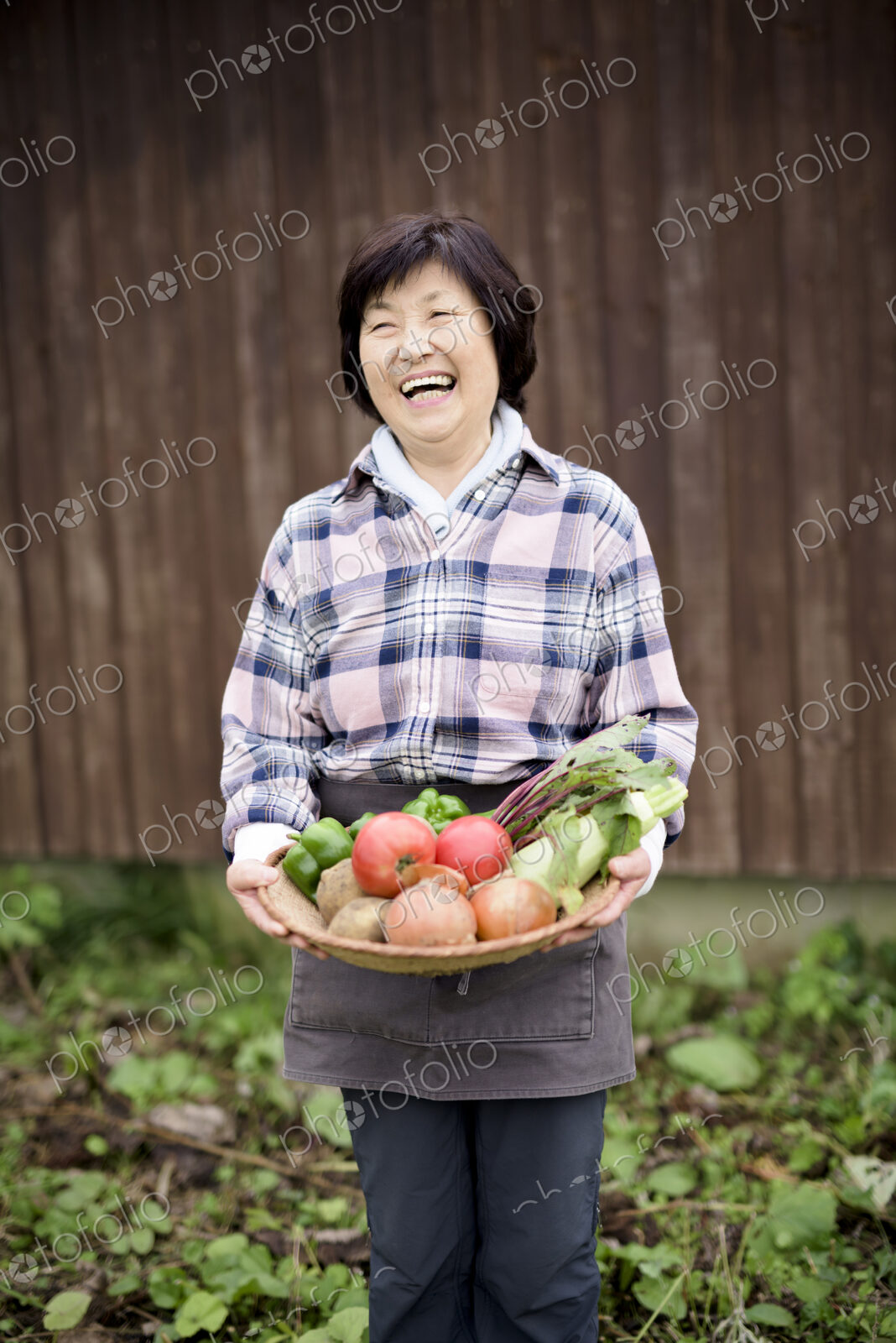 Woman with black hair wearing checkered shirt standing in a garden, holding basket…