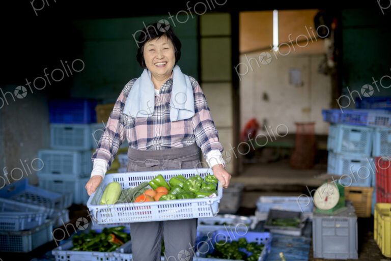 Woman with black hair wearing checkered shirt standing in front of barn, holding blue…