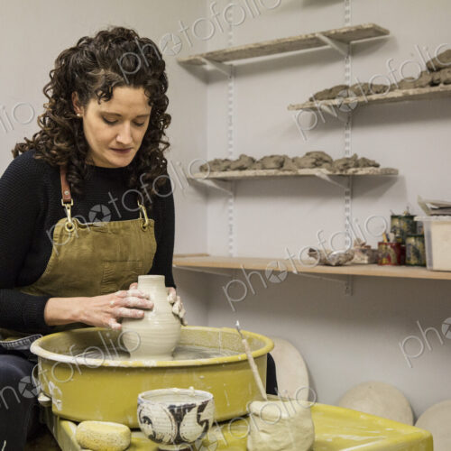 Woman with brown curly hair wearing apron shaping clay vase on pottery wheel. Woman with brown curly hair wearing apron shaping clay vase on pottery wheel.