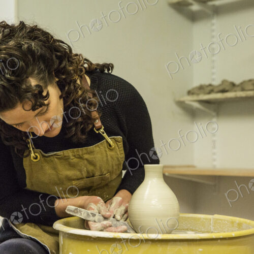 Woman with brown curly hair wearing apron shaping clay vase on pottery wheel. Woman with brown curly hair wearing apron shaping clay vase on pottery wheel.