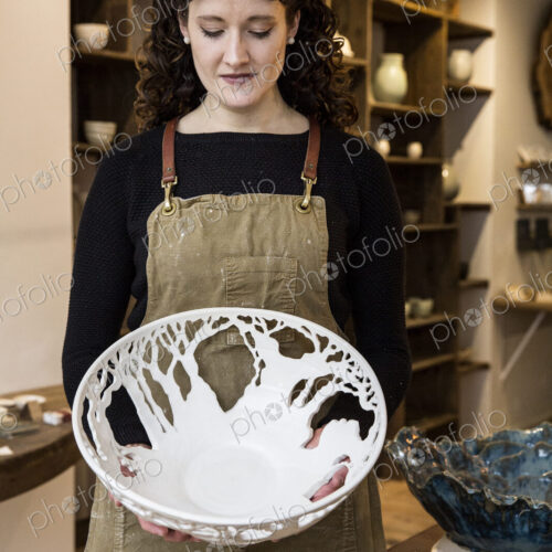 Woman with curly brown hair wearing apron holding a large intricate white ceramic bowl. Woman with curly brown hair wearing apron holding a large intricate white ceramic bowl.