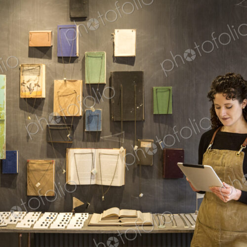 Woman with curly brown hair wearing apron standing in her pottery shop, looking at… Woman with curly brown hair wearing apron standing in her pottery shop, looking at…