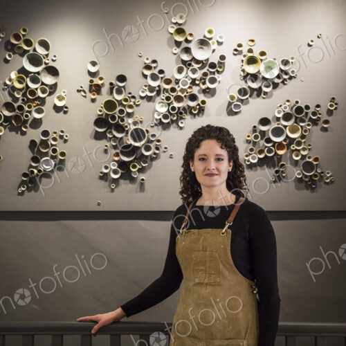 Woman with curly brown hair wearing apron standing in her pottery shop, smiling at camera. Woman with curly brown hair wearing apron standing in her pottery shop, smiling at camera.