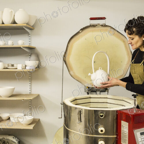Woman with curly brown hair wearing apron standing in pottery workshop, placing vase… Woman with curly brown hair wearing apron standing in pottery workshop, placing vase…