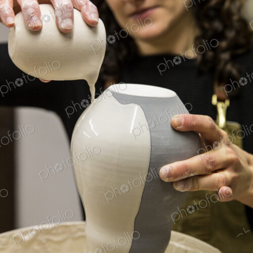 Woman with curly brown hair wearing apron standing in pottery workshop, pouring white… Woman with curly brown hair wearing apron standing in pottery workshop, pouring white…