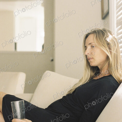 Woman with long blond hair wearing a black dress, sitting on a sofa, holding a glass. Woman with long blond hair wearing a black dress, sitting on a sofa, holding a glass.