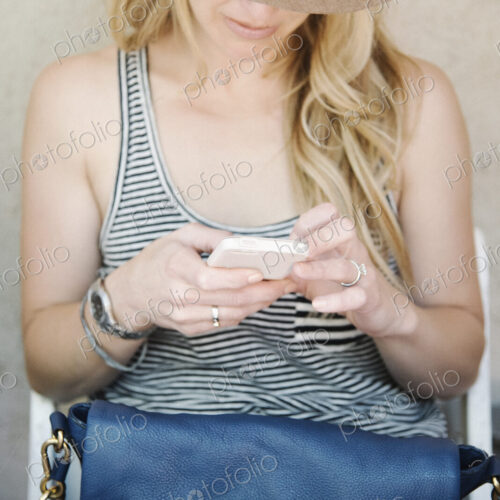 Woman with long blond hair, wearing a hat, looking down at her cell phone. Woman with long blond hair, wearing a hat, looking down at her cell phone.