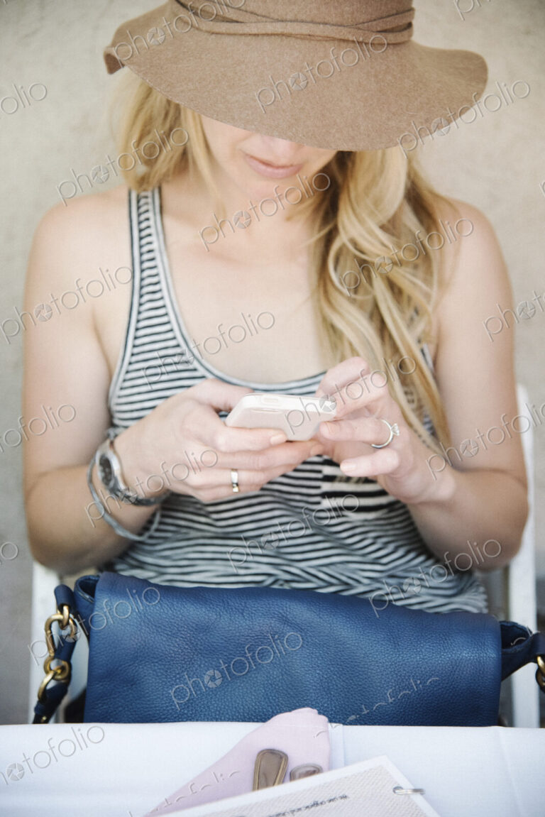 Woman with long blond hair, wearing a hat, looking down at her cell phone.