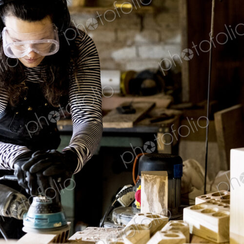Woman with long brown hair wearing dungarees, safety glasses and ear protectors…