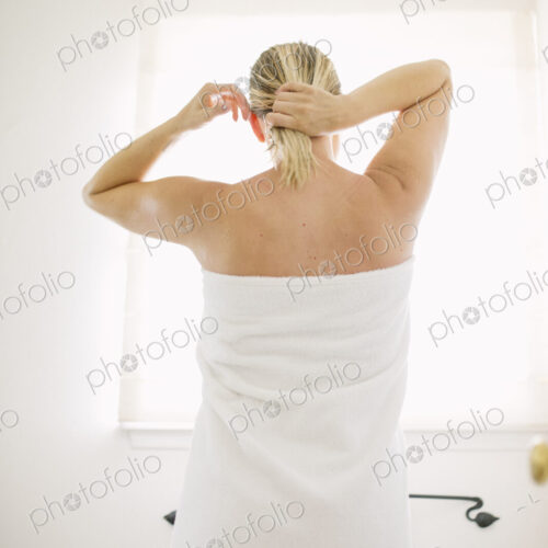 Woman wrapped in a white towel standing in a bathroom, tying her wet hair. Woman wrapped in a white towel standing in a bathroom, tying her wet hair.