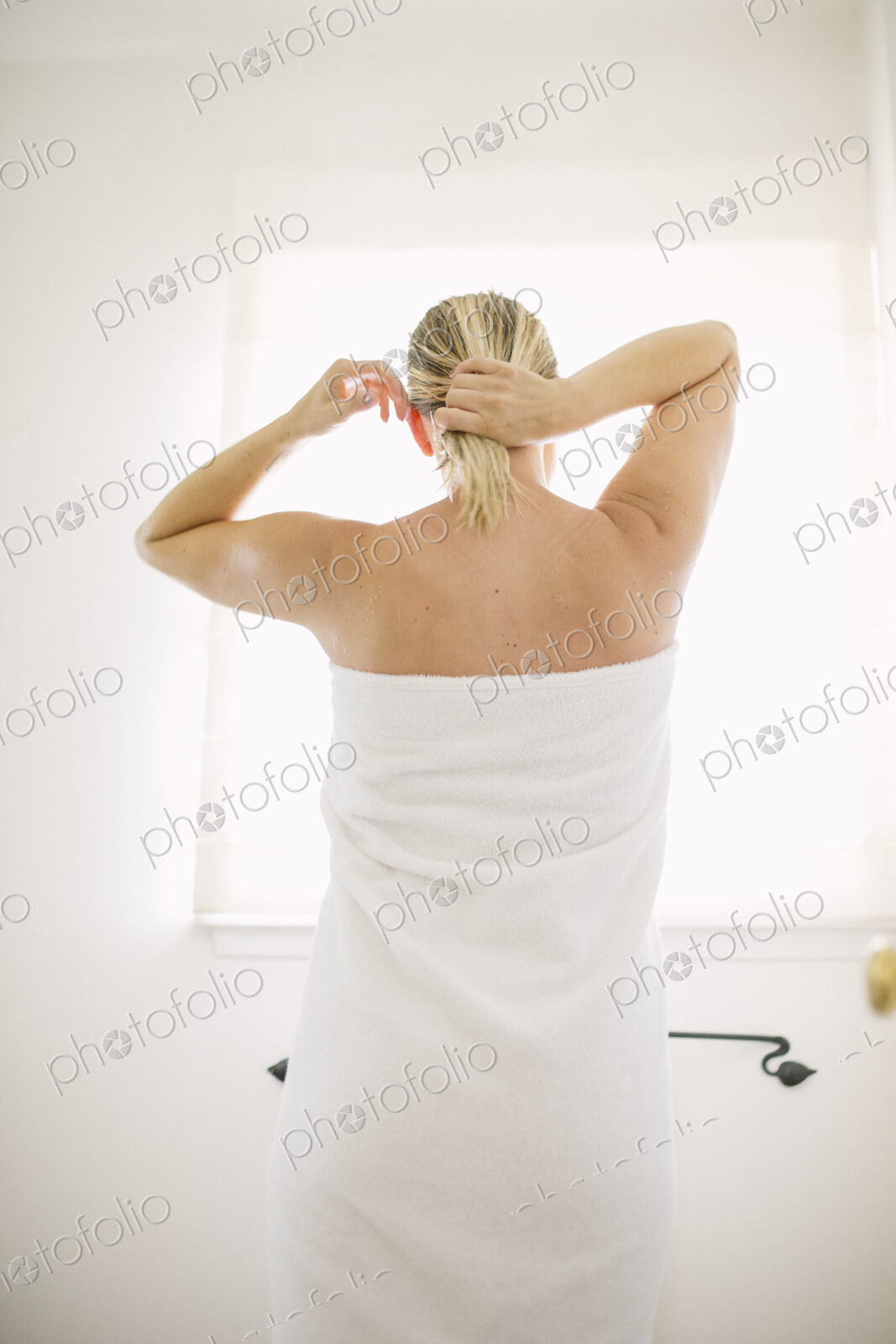 Woman wrapped in a white towel standing in a bathroom, tying her wet hair.
