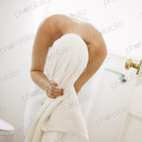 Woman wrapped in a white towel standing in a bathroom, wrapping her hair in a towel. Woman wrapped in a white towel standing in a bathroom, wrapping her hair in a towel.