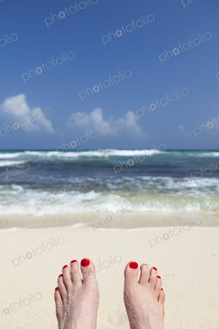 Woman's feet with red nail polish, resting on beach in Tulum, Mexico, facing turquoise…