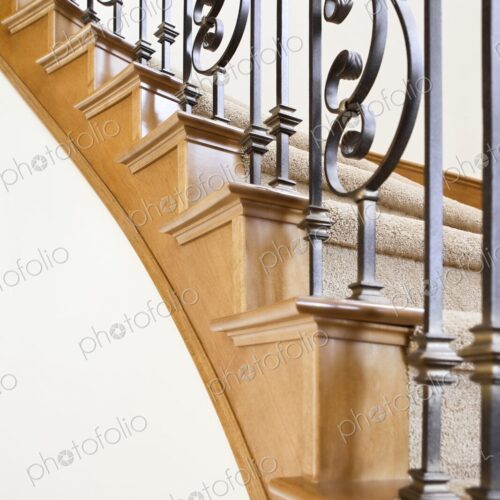 Wood and wrought iron detail of curved staircase in luxury home leading upstairs to… Wood and wrought iron detail of curved staircase in luxury home leading upstairs to…