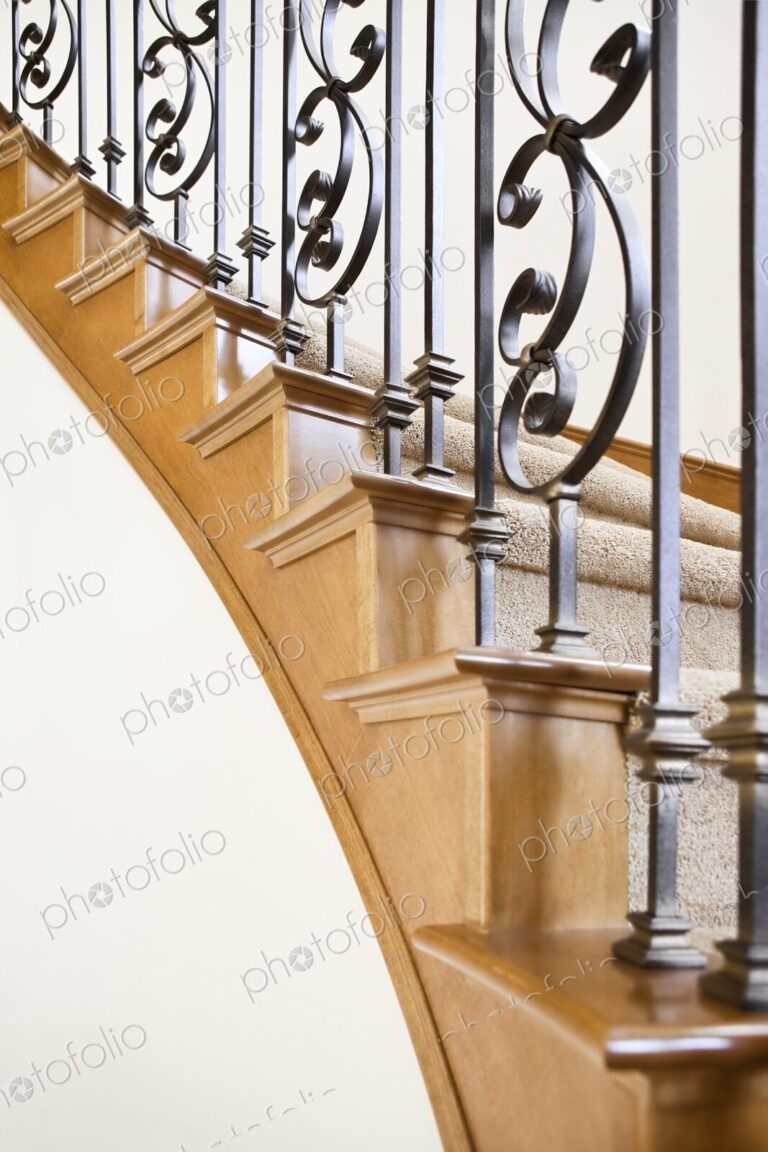 Wood and wrought iron detail of curved staircase in luxury home leading upstairs to…