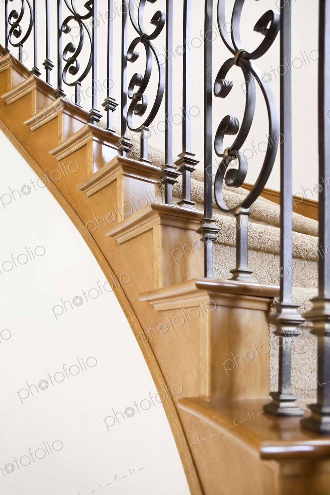 Wood and wrought iron detail of curved staircase in luxury home leading upstairs to…