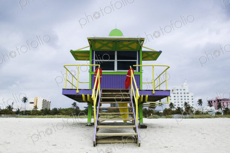 Wooden colourful lifeguard hut on a sandy beach with high rise buildings beyond.