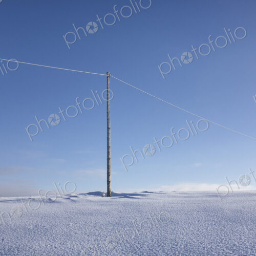 Wooden electric pole on empty snow covered landscape. Electrical industry, power line.
