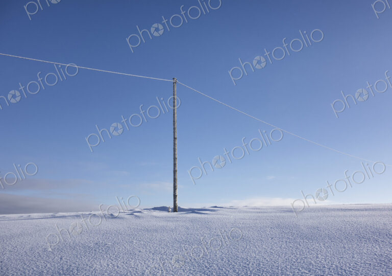 Wooden electric pole on empty snow covered landscape. Electrical industry, power line.