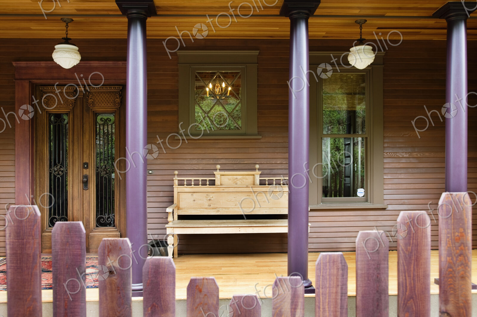 Wooden fence and house porch with columns and bench.