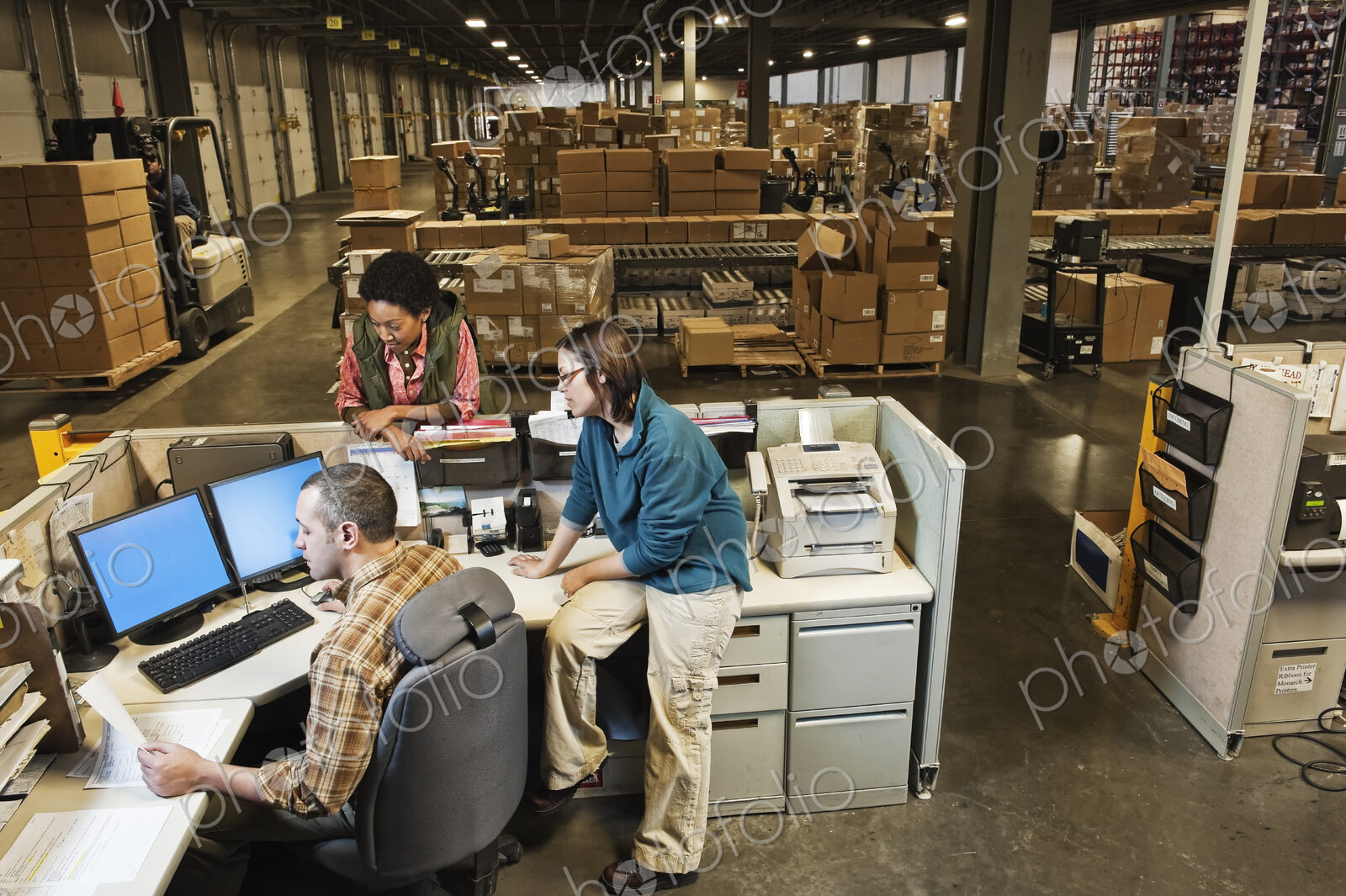 Workers studing a document on a computer at the front desk of a distribution warehouse.