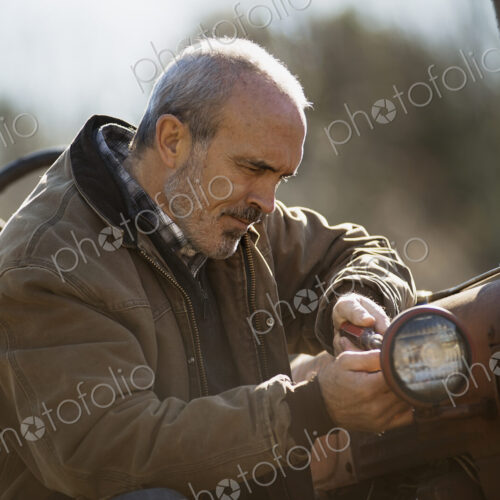 Working on an organic farm. A man in a brown jacket working on farm equipment. A tractor. Working on an organic farm. A man in a brown jacket working on farm equipment. A tractor.