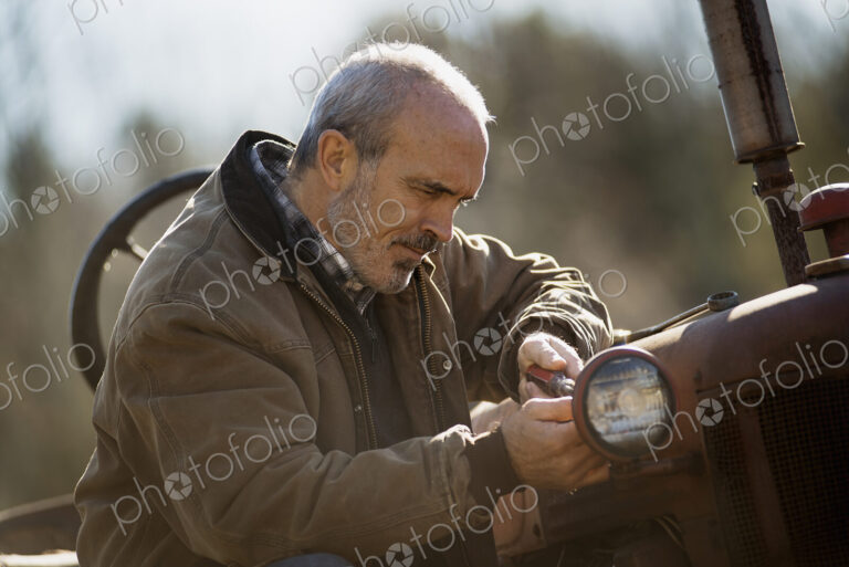 Working on an organic farm. A man in a brown jacket working on farm equipment. A tractor.