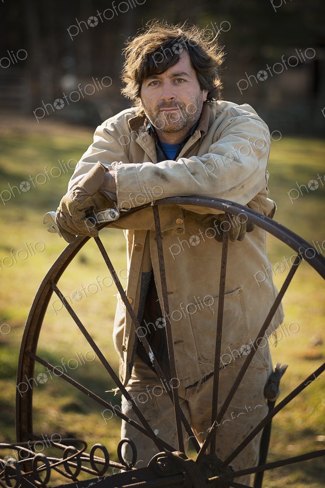 Working on an organic farm. A man in overalls wearing work gloves, leaning on a round…