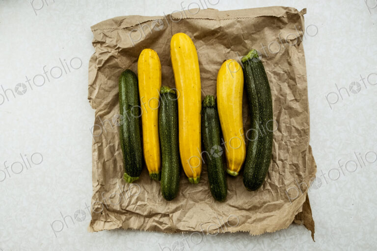 Yellow and green courgettes displayed on a crumpled brown paper bag.