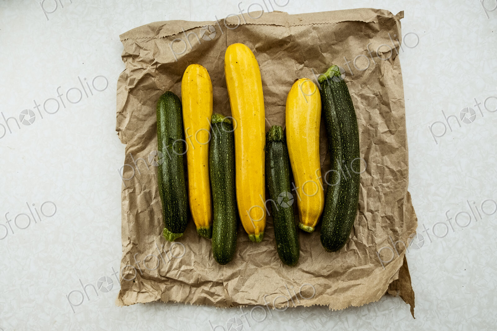 Yellow and green courgettes displayed on a crumpled brown paper bag.
