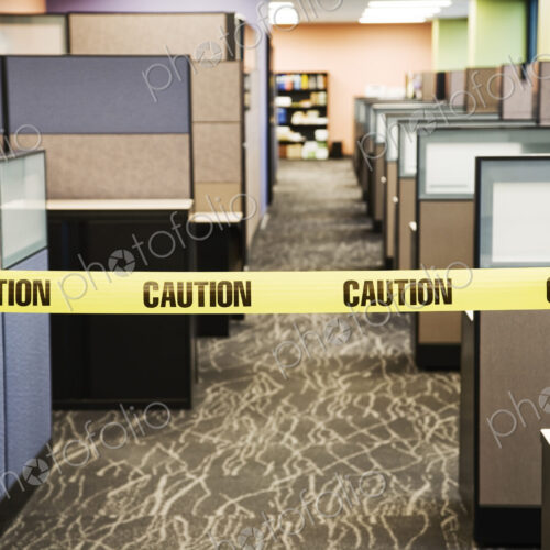 Yellow caution tape stretched between cubicles in an office space. Yellow caution tape stretched between cubicles in an office space.