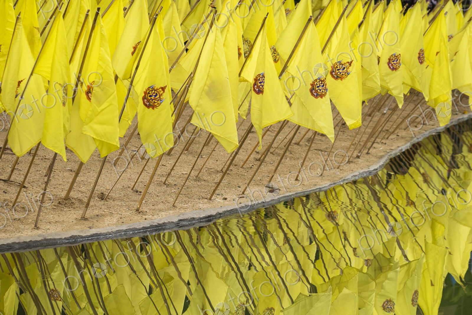 Yellow prayer flags stuck in sand over reflecting water at a wat temple.