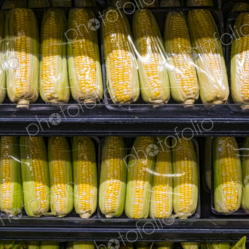 Yellow sweetcorn husks packaged in plastic on a supermarket shelf. Yellow sweetcorn husks packaged in plastic on a supermarket shelf.