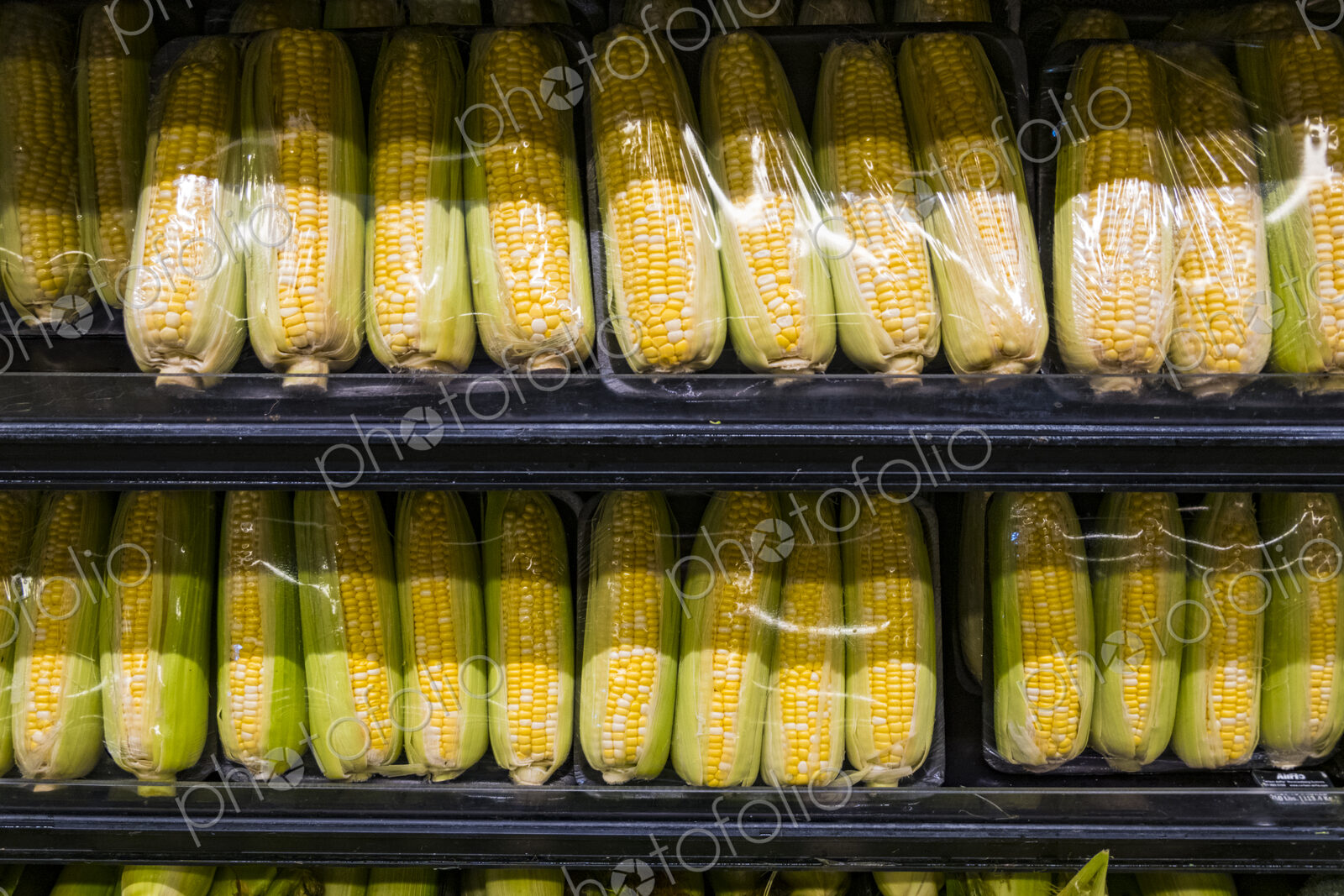 Yellow sweetcorn husks packaged in plastic on a supermarket shelf.
