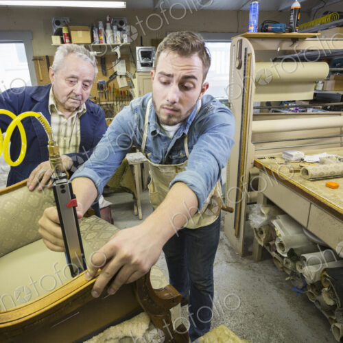 Young Caucasian man learning the art of upholsery from a senior male upholsterer. Young Caucasian man learning the art of upholsery from a senior male upholsterer.