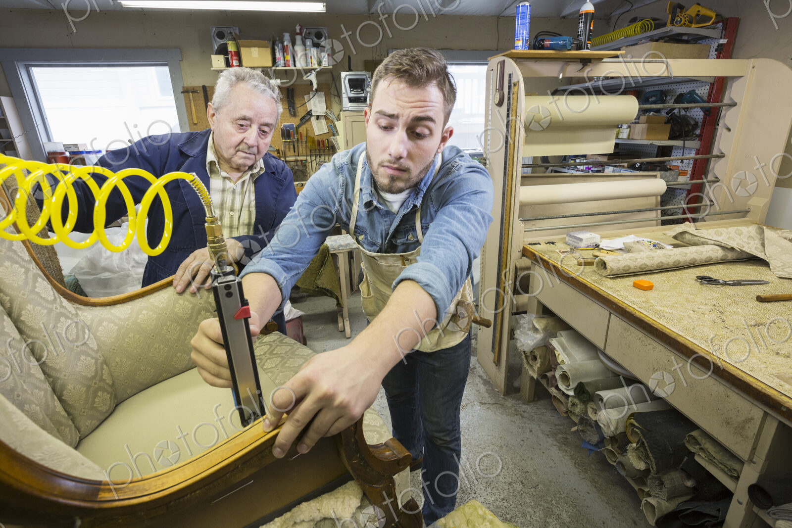 Young Caucasian man learning the art of upholsery from a senior male upholsterer.
