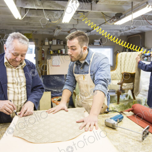 Young Caucasian man learning the art of upholstery from a senior male upholsterer.