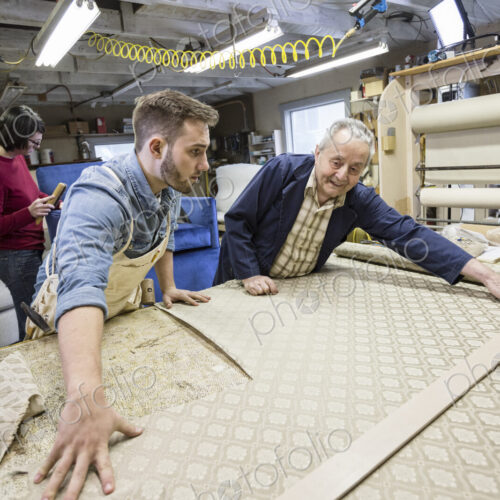 Young Caucasian man learning the art of upholstery from a senior male upholsterer.