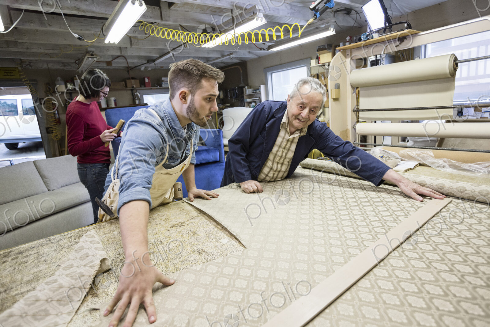 Young Caucasian man learning the art of upholstery from a senior male upholsterer.