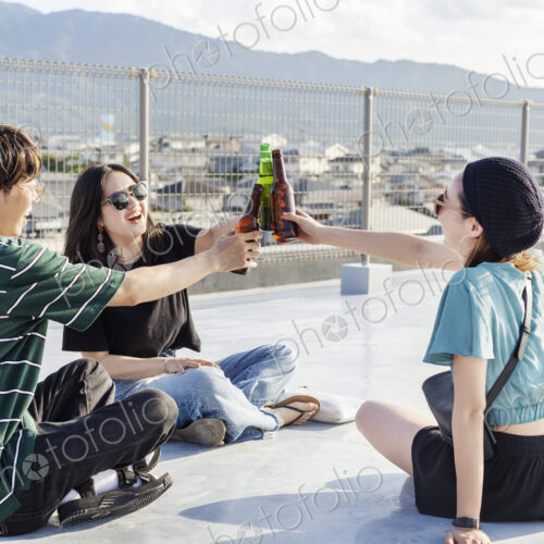 Young Japanese man and two women sitting on a rooftop in an urban setting, drinking beer. Young Japanese man and two women sitting on a rooftop in an urban setting, drinking beer.