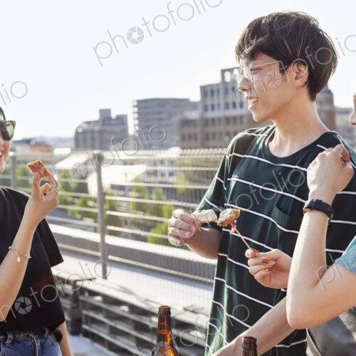 Young Japanese man and two women standing on a rooftop in an urban setting, drinking beer. Young Japanese man and two women standing on a rooftop in an urban setting, drinking beer.